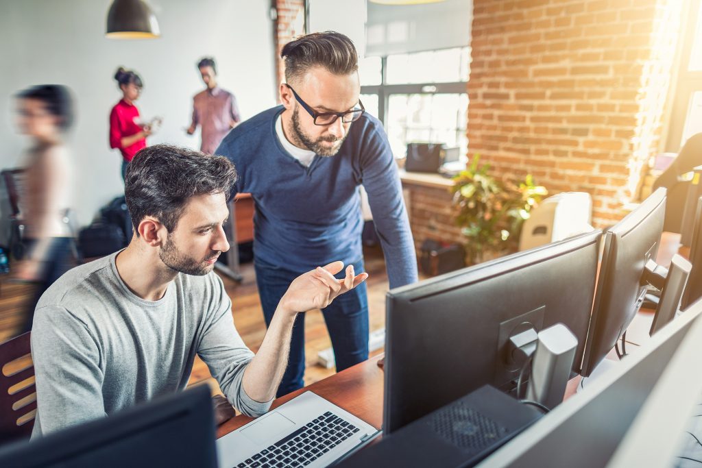 Two men in an office working at a computer having questions for their IT outsourcing company